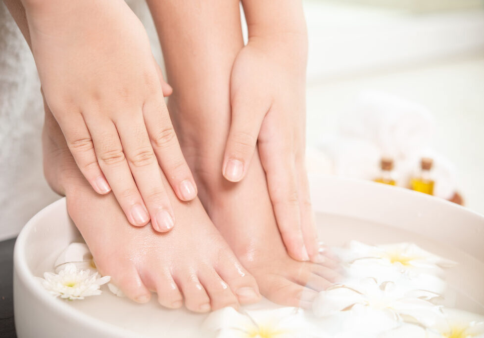 closeup view of woman soaking her hand and feet in dish with water and flowers on wooden floor. Spa treatment and product for female feet and hand spa. white flowers in ceramic bowl.