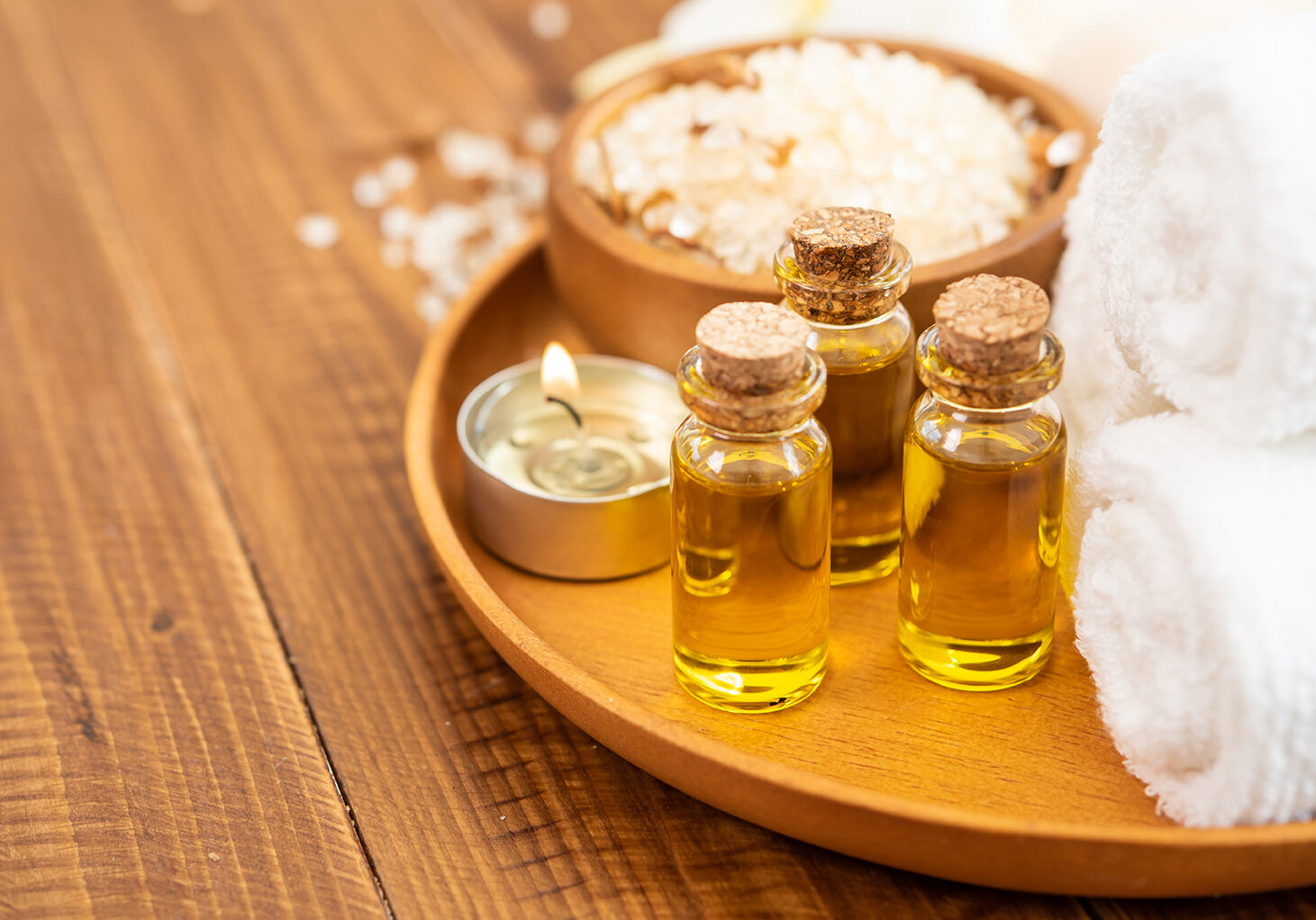 Sea salt, towels, aroma oil in bottles and flowers on vintage wooden background. Selective focus.